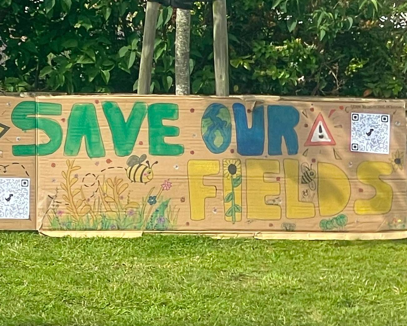 Hand-painted "Save Our Fields" banner made by local children, decorated with a globe, bees, sunflowers and wildflowers